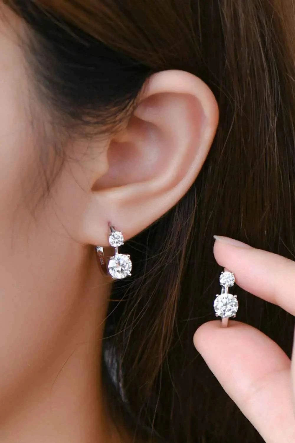 1.3 Carat Moissanite sterling silver earrings with two round clear stones, one worn and one held by hand