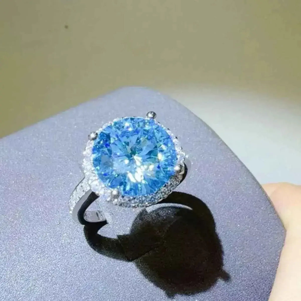 1 Carat Moissanite silver ring featuring a large round blue stone surrounded by smaller clear stones on a polished band