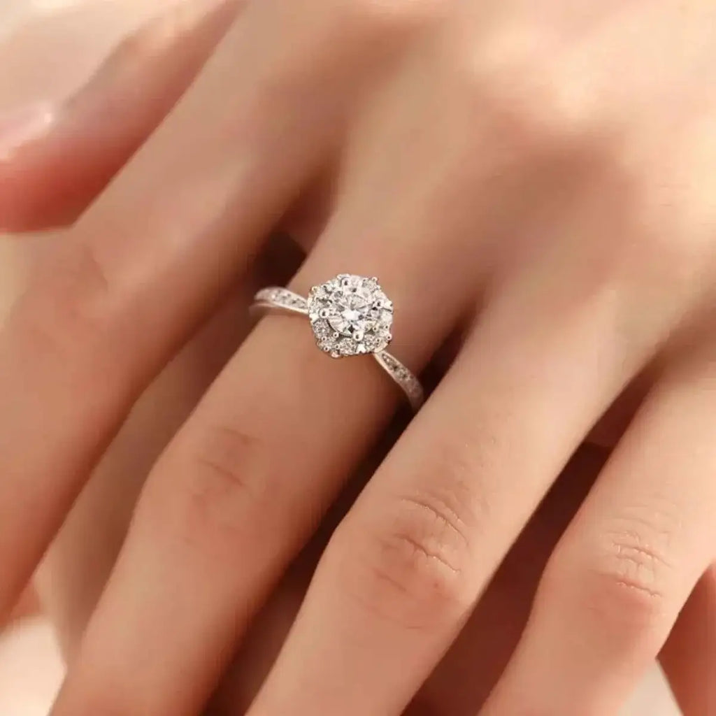 1 Carat Moissanite sterling silver ring featuring a round central stone surrounded by smaller stones on a delicate band