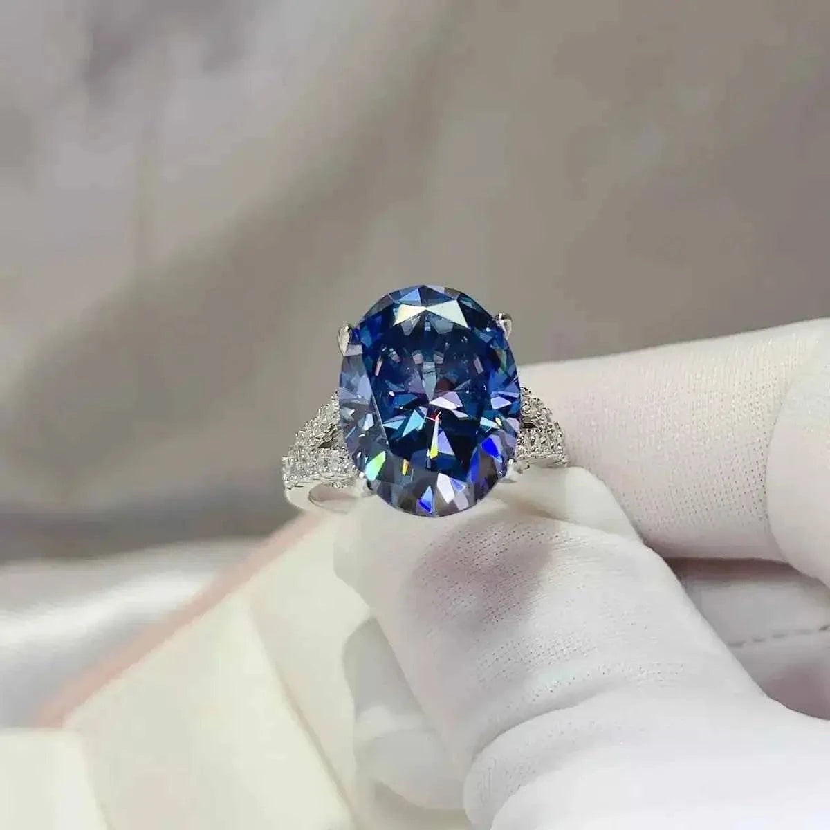 Sterling silver ring featuring a large oval blue gemstone with side diamond accents, showcasing a 10 Carat Moissanite centerpiece.