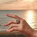 5 Carat sterling silver ring with a large central clear moissanite stone surrounded by smaller sparkling stones in a floral design