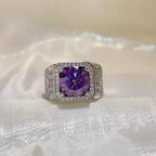 Sterling silver ring featuring a large round purple stone surrounded by smaller clear stones, ornate band design, 5 Carat Moissanite