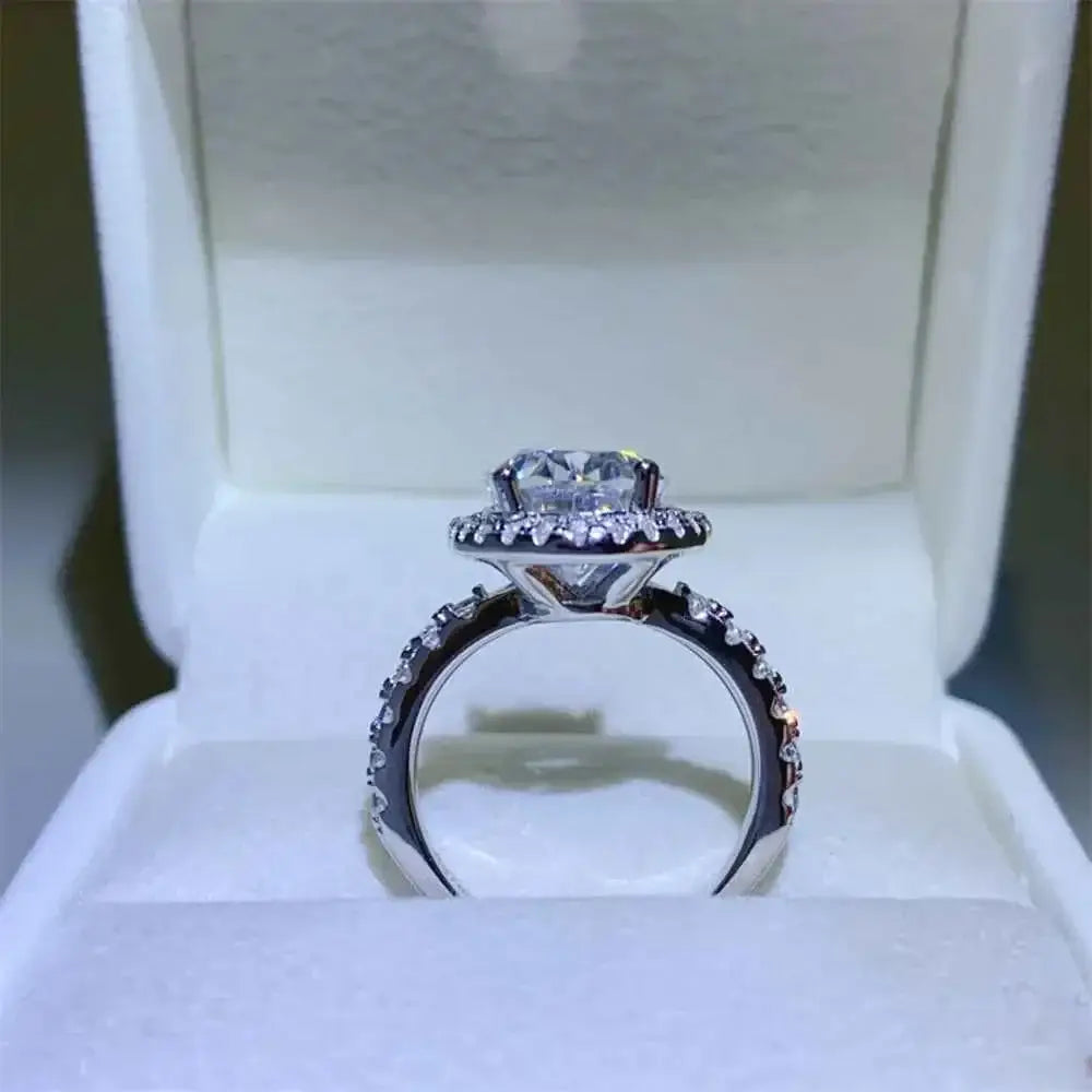 925 sterling silver ring featuring a round 5 Carat Moissanite center stone with smaller accent stones on the band and halo setting