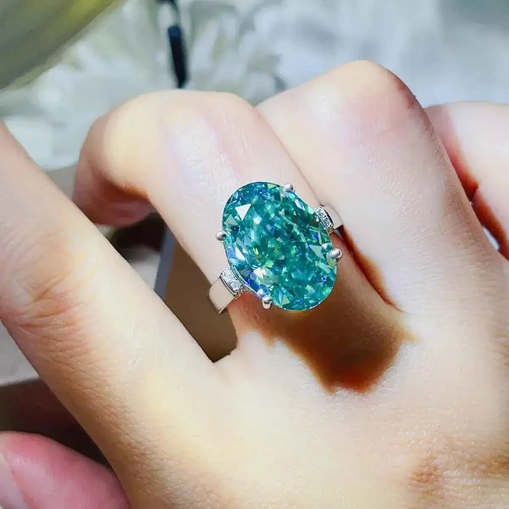Silver ring with an oval teal gemstone set in a simple band, showcasing a 5 Carat Moissanite centerpiece with platinum plating.