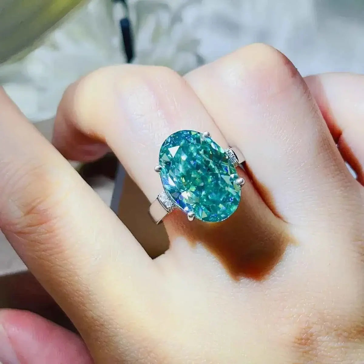 Silver ring with an oval teal gemstone set in a simple band, showcasing a 5 Carat Moissanite centerpiece with platinum plating.