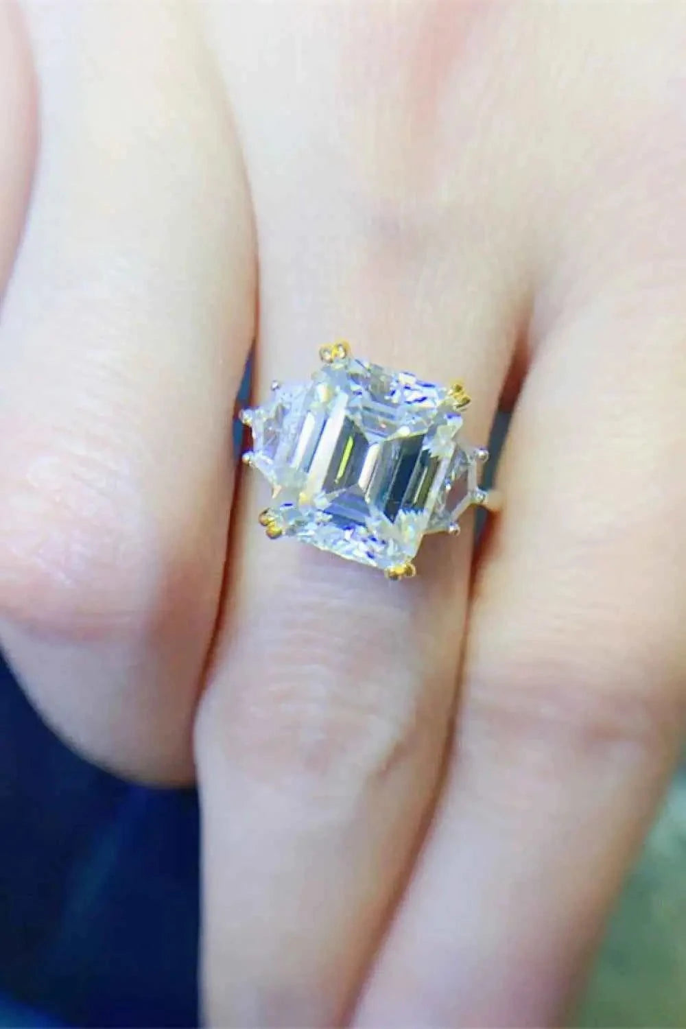 925 sterling silver ring with a large emerald-cut 5 Carat Moissanite stone and gold prong settings on a finger