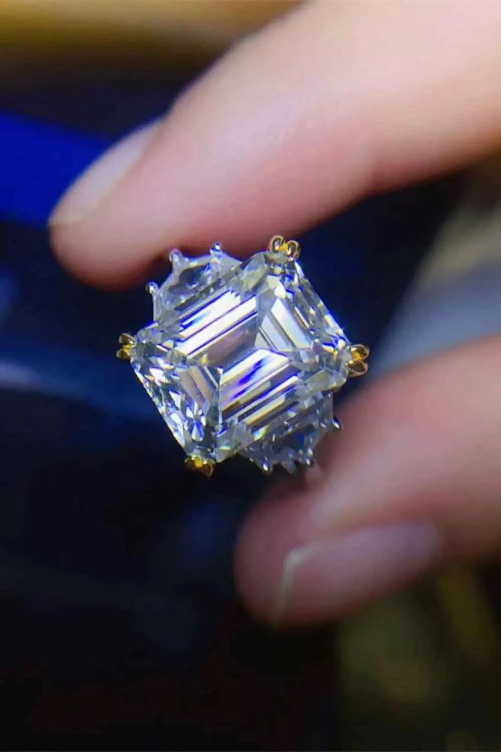 Close-up of a 5 Carat Moissanite square-cut gemstone held between fingers, set in a platinum-plated 925 sterling silver ring with gold prongs.