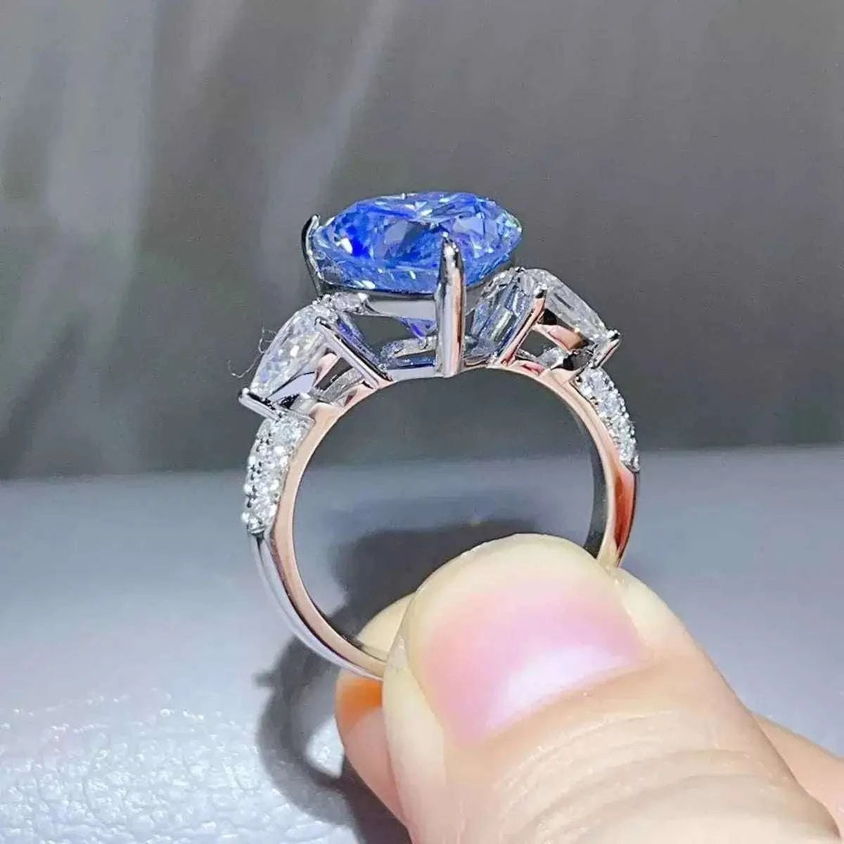 6 Carat sterling silver ring featuring a prominent blue heart-shaped moissanite center stone with side clear stones and pavé accents