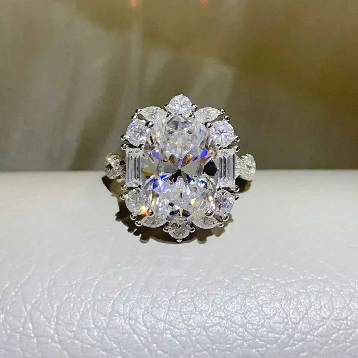 Moissanite ring featuring a large oval center stone surrounded by smaller round and baguette stones in Carat 925 Sterling Silver setting.