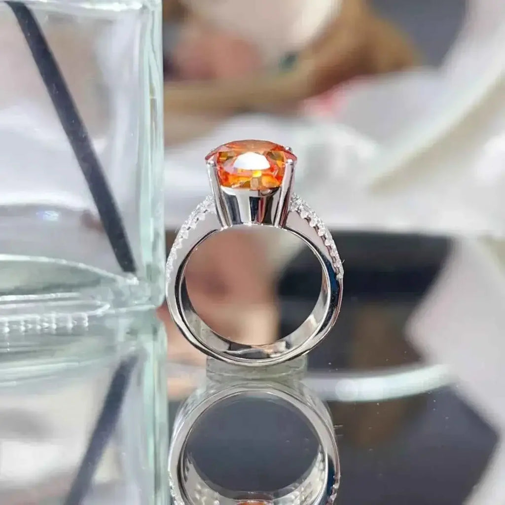 925 sterling silver ring with a large orange 8 Carat Moissanite center stone and small clear side stones on the band