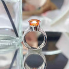 925 sterling silver ring with a large orange 8 Carat Moissanite center stone and small clear side stones on the band