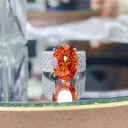 925 sterling silver ring with a large oval orange 8 Carat Moissanite center stone surrounded by pavé clear stones on the band