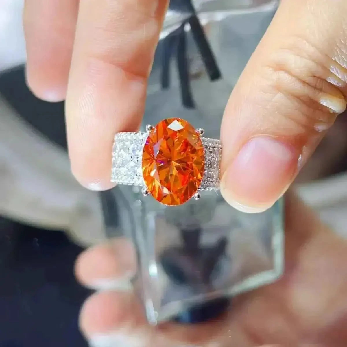 8 Carat Moissanite ring with a large oval orange stone set in a platinum-plated 925 sterling silver band encrusted with small clear stones.