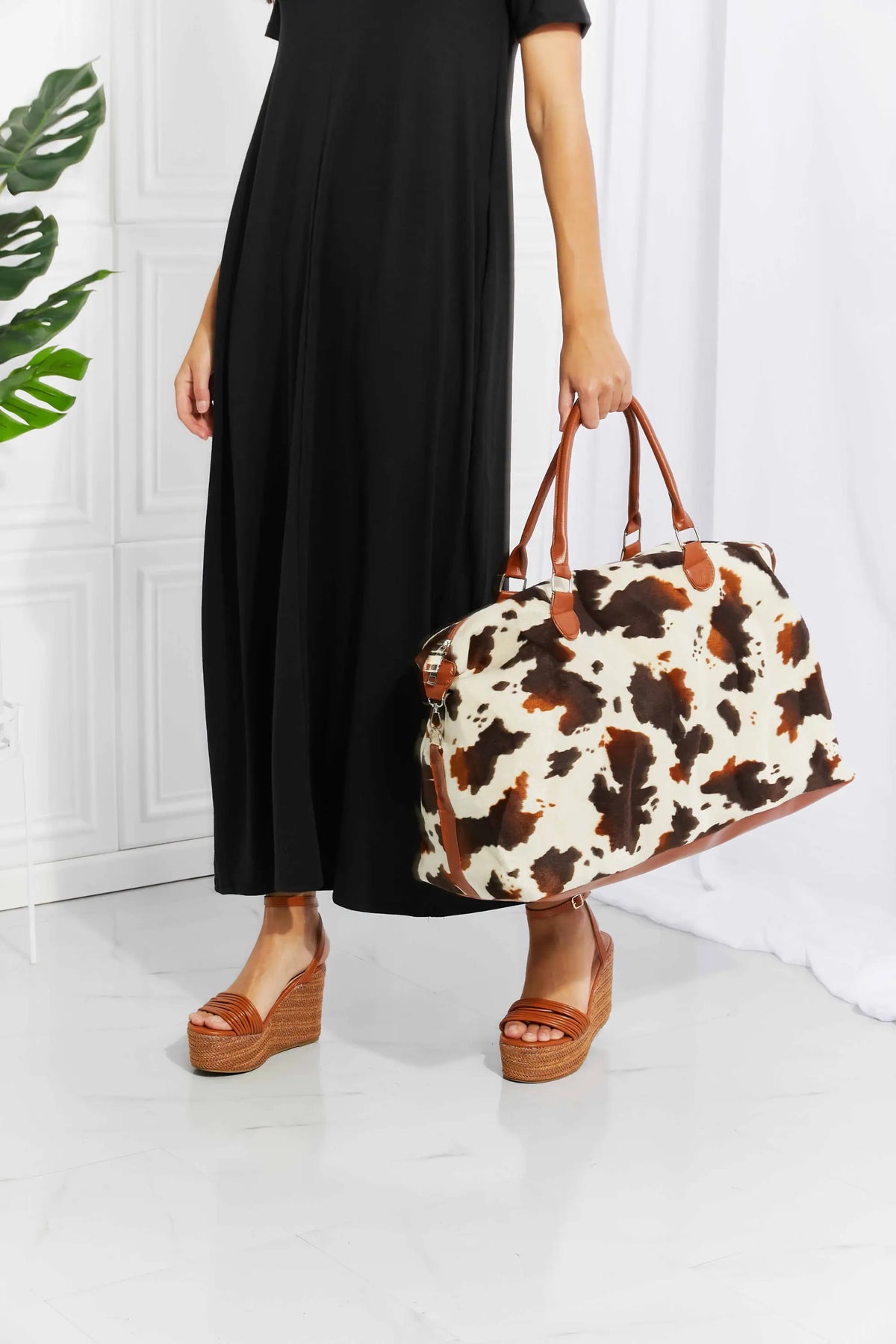 Animal Print Plush medium weekender bag with brown and black cow pattern, fluff material, and brown top handles held by person