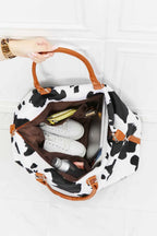Animal Print Plush weekender bag in black and white cow pattern with brown top handles and open zipper showing interior items