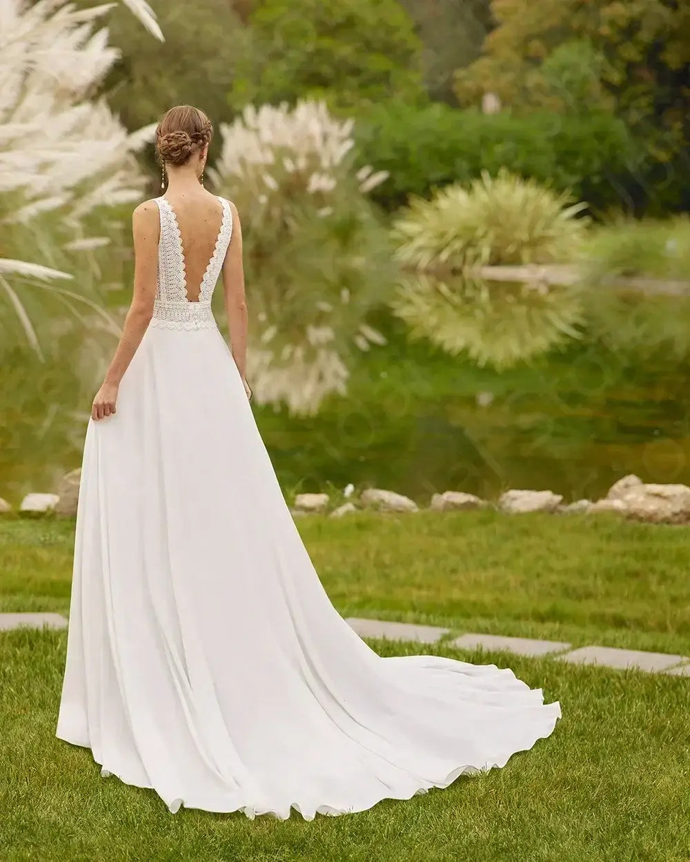 Beach Wedding Dress in white flowing fabric with lace detailing and deep backless design, court train draping on grass