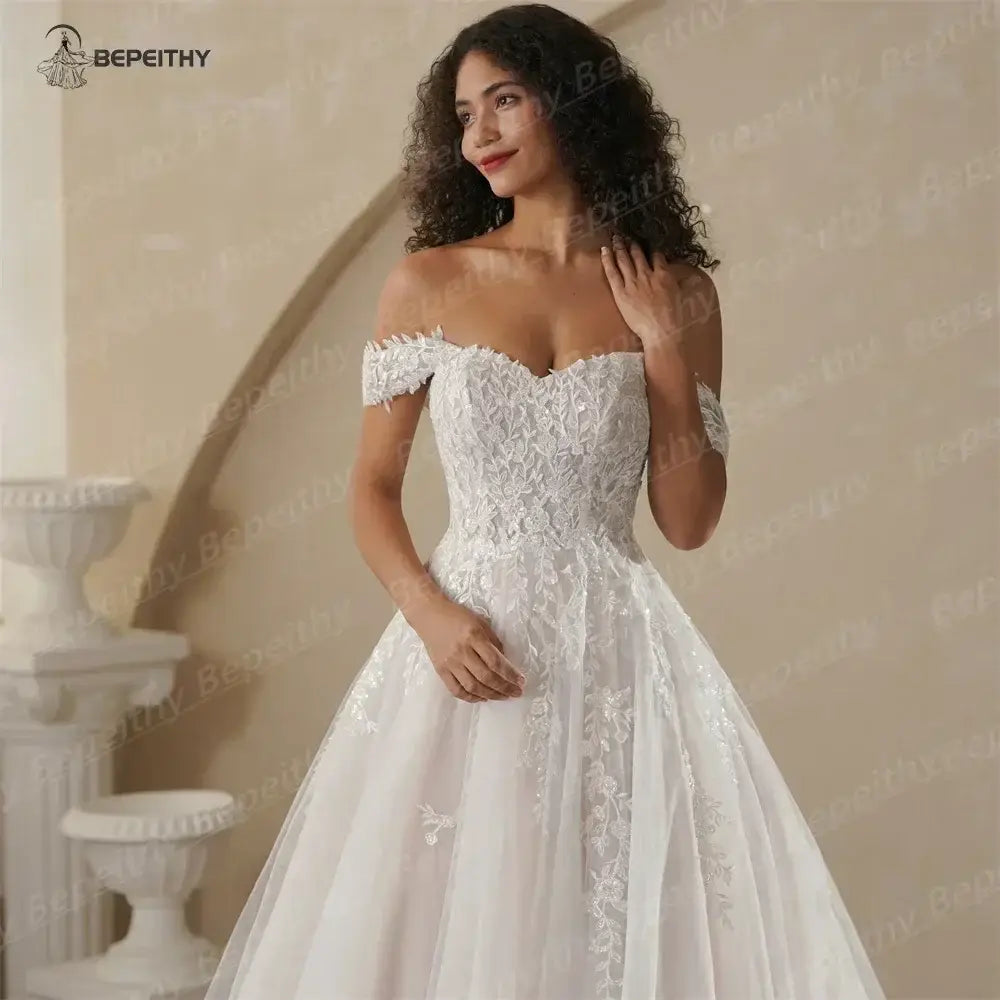 Boho Champagne Wedding Dress in off-shoulder white lace with floral appliques and an A-line silhouette on model