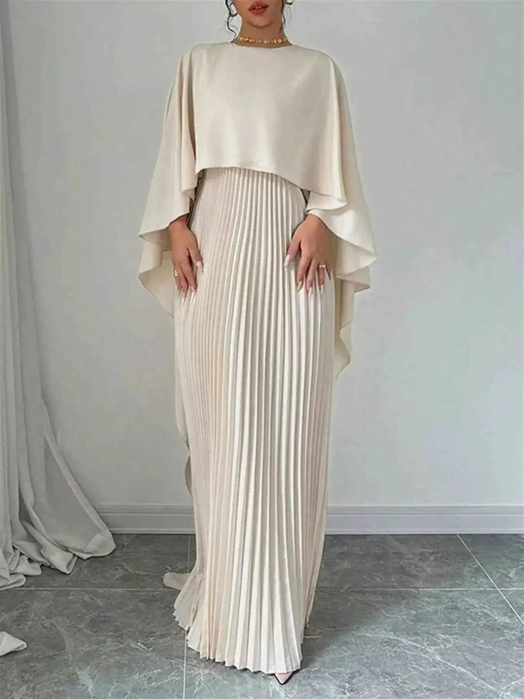 Cape Pleated Maxi Dress in cream polyester with a flowing cape overlay and finely pleated maxi skirt design.