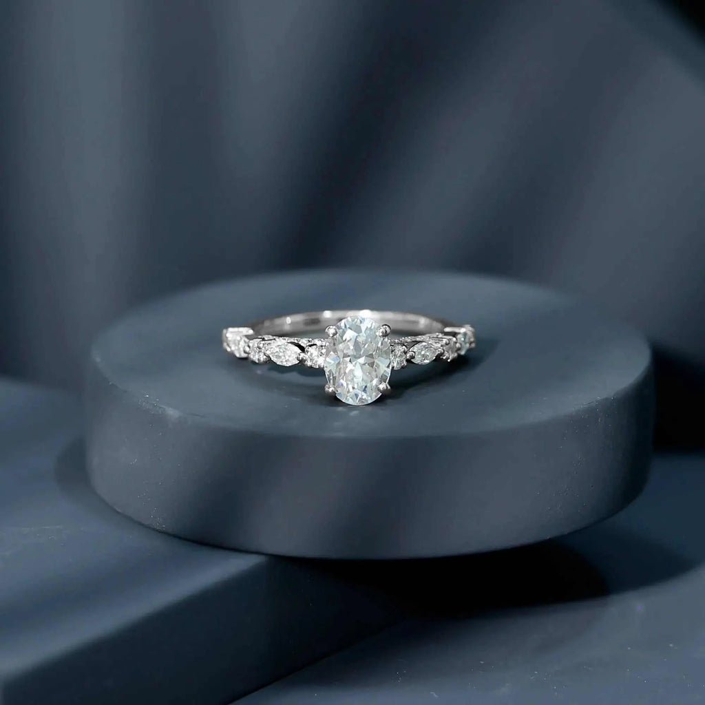 Silver engagement ring featuring a Carat IGI Certified Oval Diamond center stone with round and marquise side stones on a sleek band