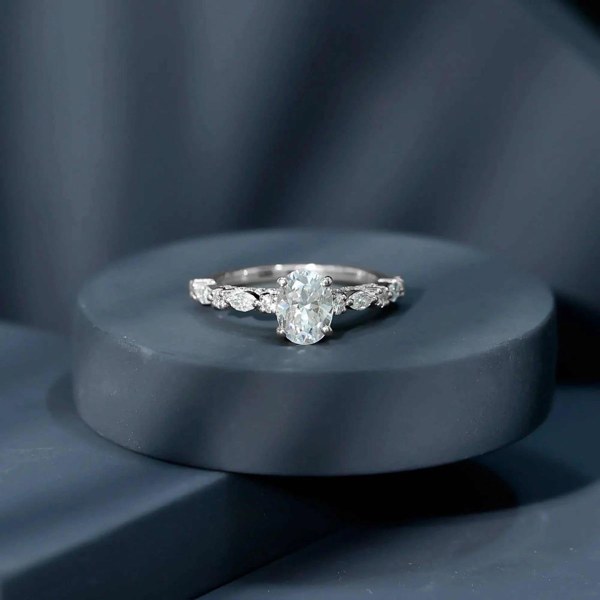 Silver engagement ring featuring a Carat IGI Certified Oval Diamond center stone with round and marquise side stones on a sleek band