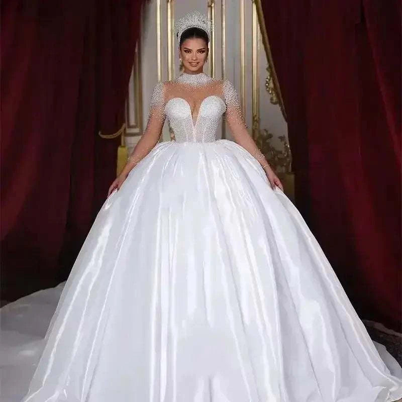 White lustrous satin ball gown wedding dress with full long sheer sleeves adorned with pearls and a high neckline