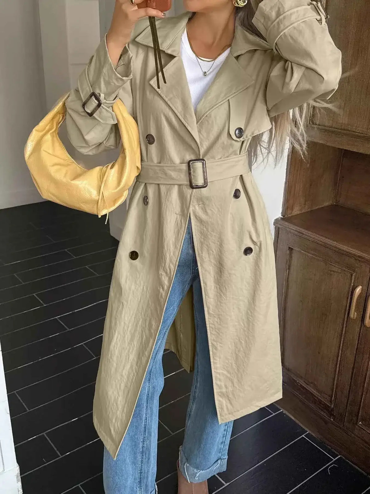 Double-Breasted Belted Trench Coat in beige polyester with buttoned cuffs and waist belt worn over blue jeans