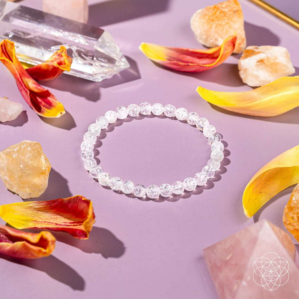 Ice Quartz bracelet with translucent 6mm crackled beads on a pastel surface surrounded by orange and yellow flower petals and crystals