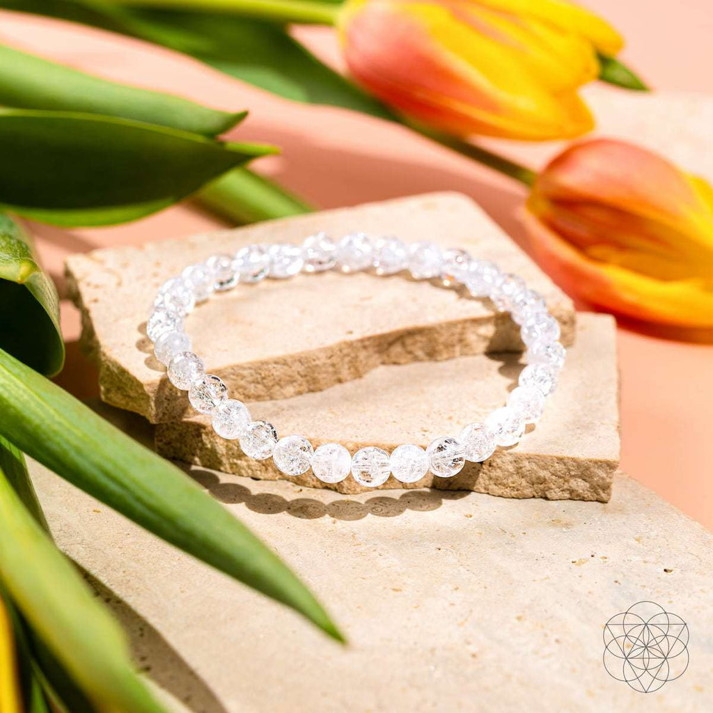 Ice Quartz bracelet composed of translucent 6mm round beads with internal fractures, displayed on natural stone with yellow and orange tulips