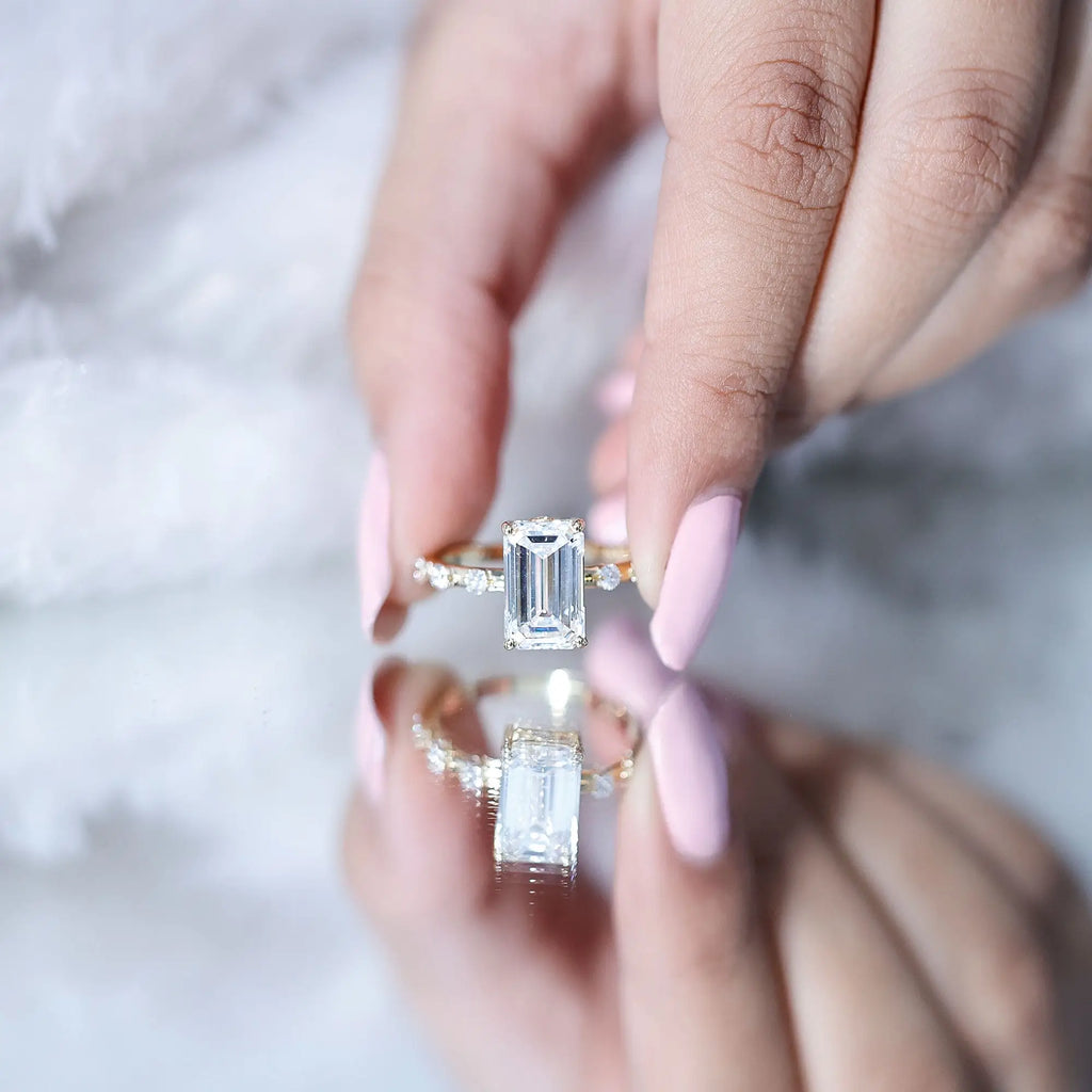 IGI Certified 4 Carat emerald cut diamond engagement ring with prong setting and spaced round accent stones on polished band