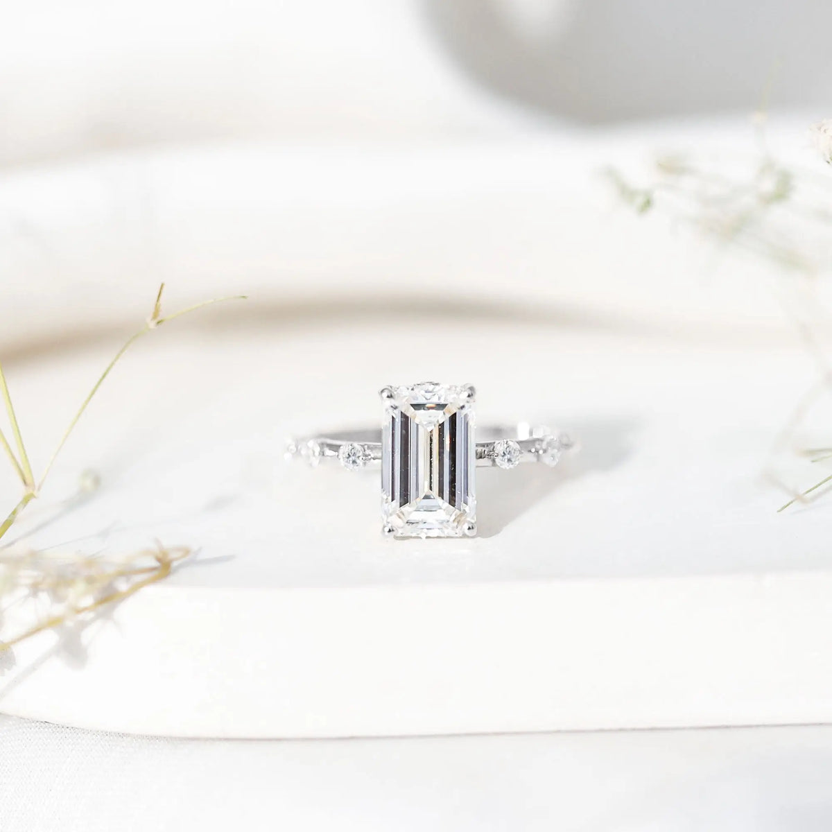 IGI Certified 4 Carat lab grown emerald cut diamond engagement ring with spaced round accent stones on a polished silver band