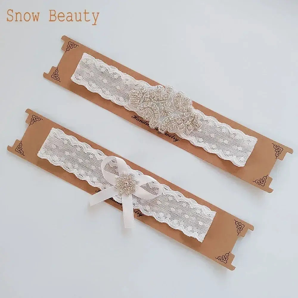 Two white lace garters with pearl and crystal flower appliques, featuring bows on one, for wedding brides