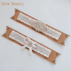 Two white lace garters with pearl and crystal flower appliques, featuring bows on one, for wedding brides
