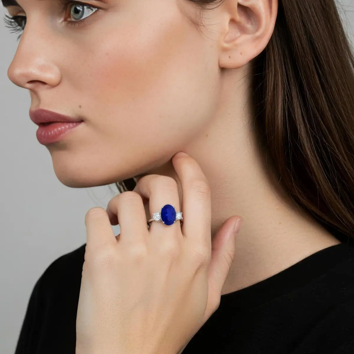 Oval lab-grown blue sapphire ring with vivid blue center stone and two round diamonds set in polished 14K white gold, worn on hand