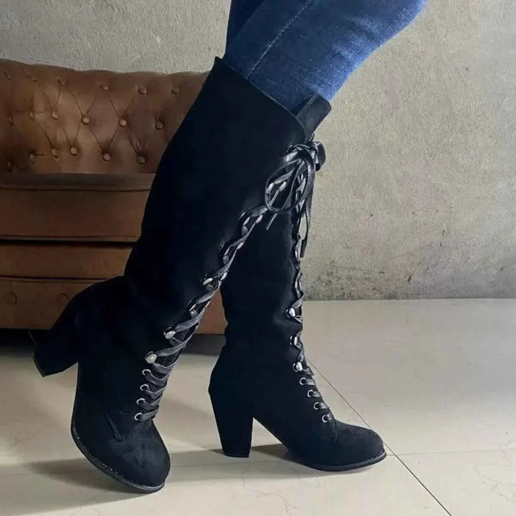 Black suede lace-up block heels boots with tall shaft and rounded toe, featuring black laces threaded through metal eyelets.