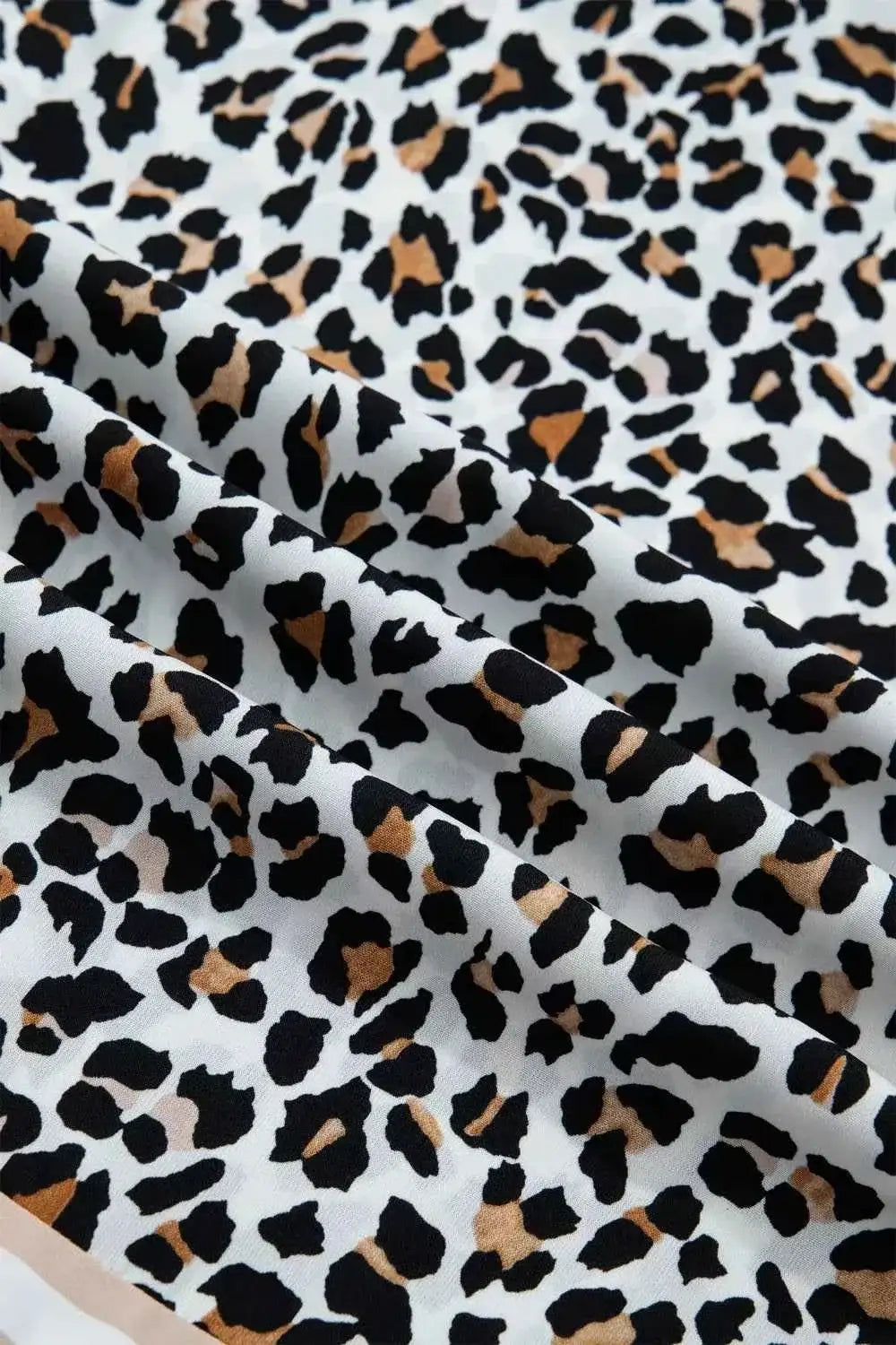 Leopard Print fabric with black and brown irregular spots on white polyester material, close-up view of sleeveless midi dress textile