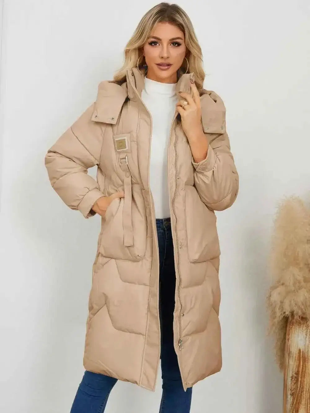Long Sleeve Longline Hooded Winter Coat in beige polyester with pockets and waist tie belt, worn with white top and blue jeans