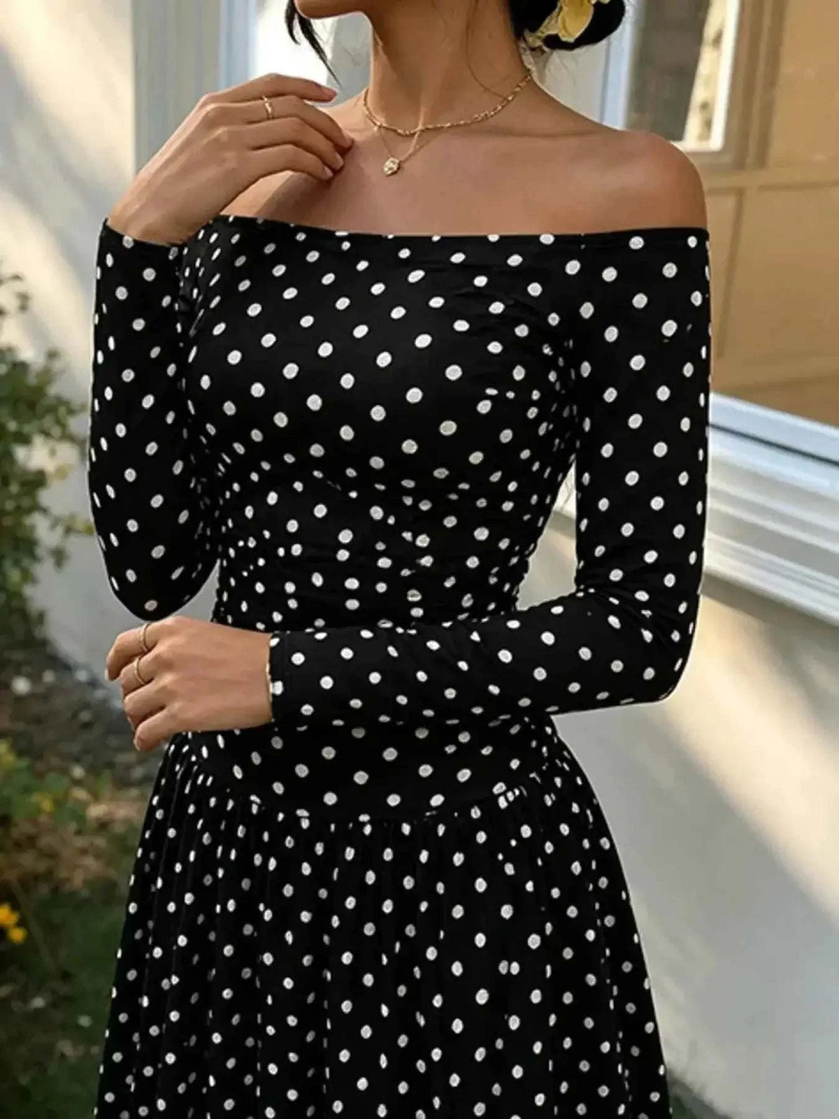 Off-the-Shoulder Maxi Dress in black with white polka dots, featuring a fitted bodice and long sleeves with an off-shoulder neckline.