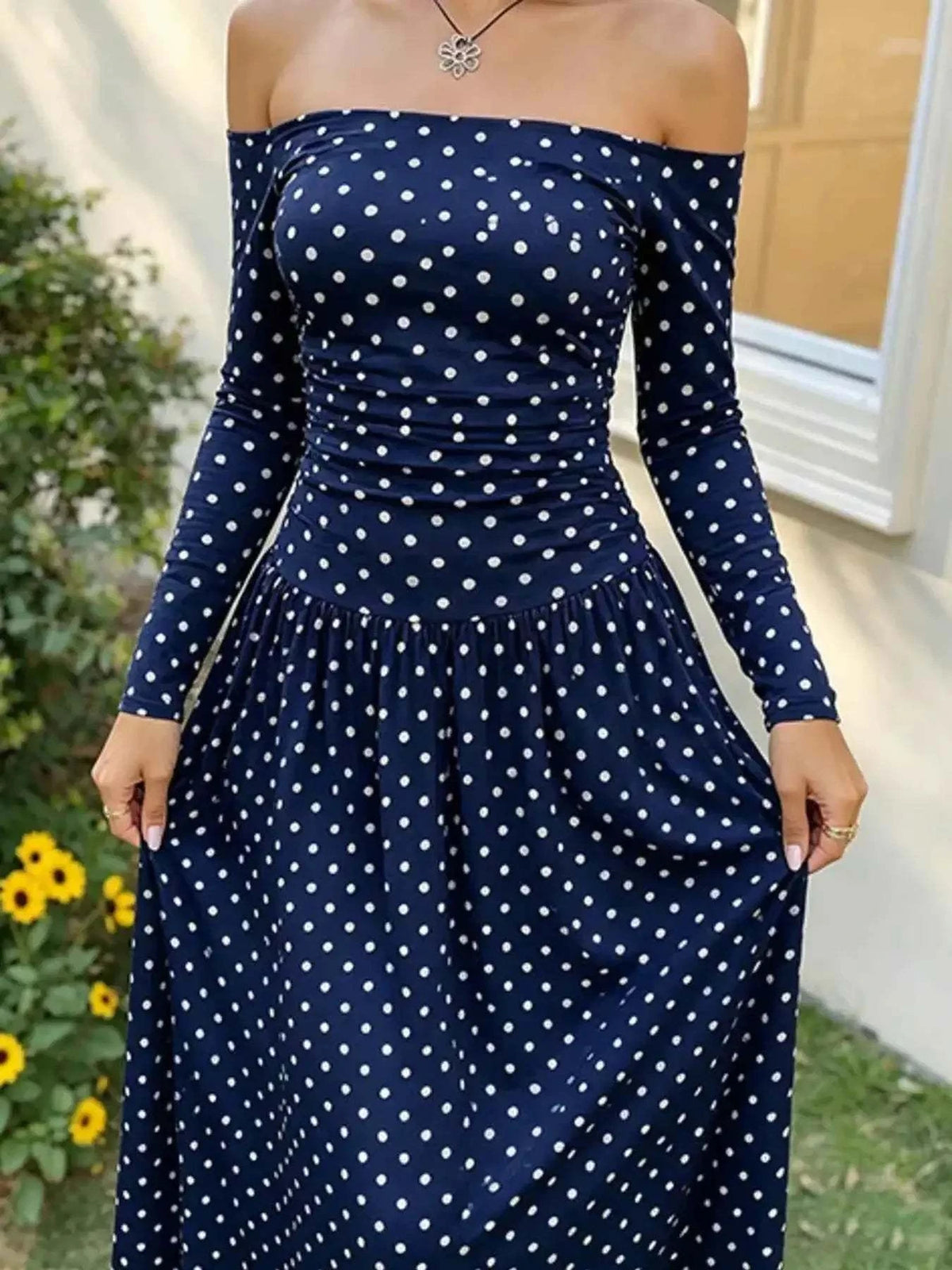 Off-the-Shoulder Maxi Dress in navy blue with white polka dots, featuring long sleeves and a fitted bodice with a flowing skirt.