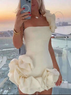 Cream one-shoulder ruffle mini dress with large cascading ruffles on shoulder and hem, fitted silhouette, slightly stretchy fabric, worn with accessories.