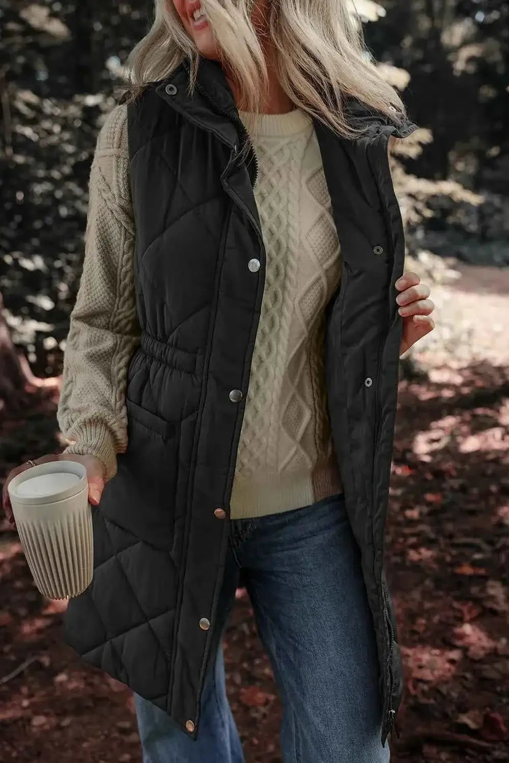 Black quilted Pocketed Zipper and Button Vest with snap buttons and side pockets, worn over a beige cable-knit sweater and blue jeans