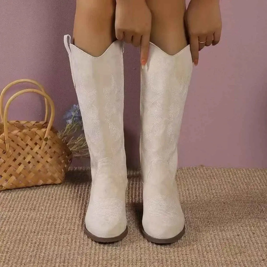 White suede knee-high boots with a subtle snake pattern and a v-shaped top, featuring Point Toe Block Heels.
