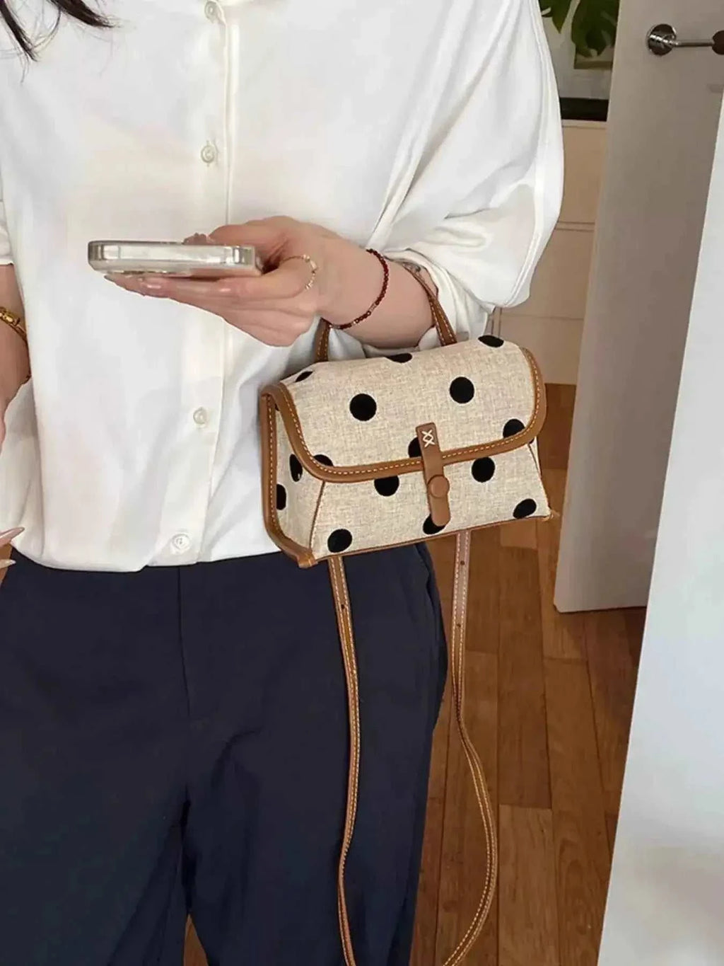 Small Polka Dot Crossbody Bag in beige polyester with black polka dots and brown trim worn with white blouse