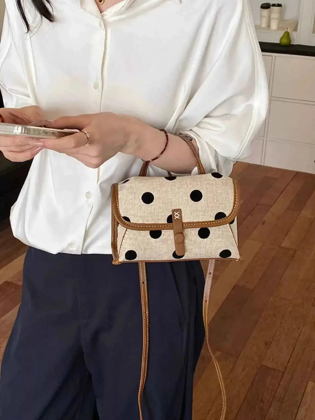 Polka Dot Crossbody Bag in beige polyester with black polka dots and brown leather trim held by person in white blouse