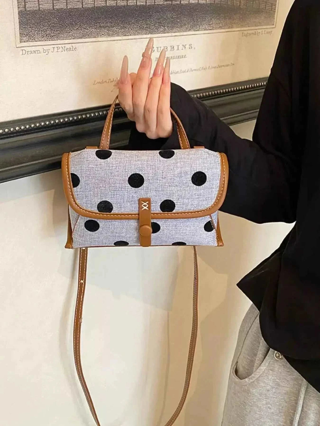 Small Polka Dot Crossbody Bag in grey polyester with large black polka dots and brown trim held by a person