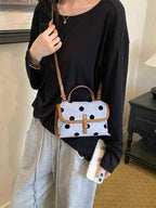 Polka Dot Crossbody Bag in white polyester with black dots and brown leather trim carried by a person in casual black and grey clothing