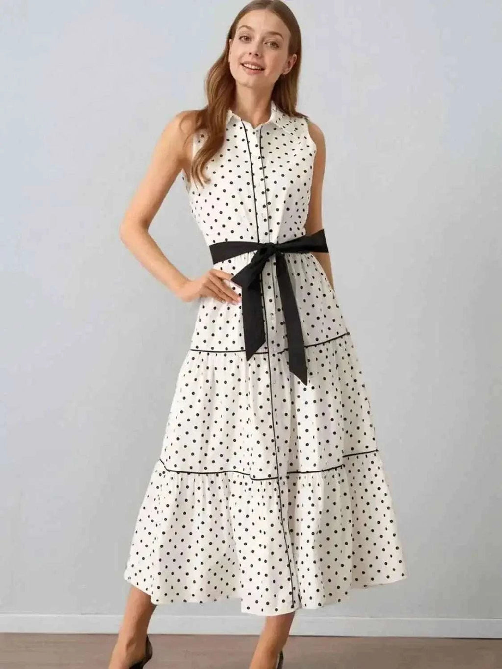 Polka Dot Sleeveless Midi Shirt Dress in white with black polka dots, featuring a buttoned front, tiered skirt, and black belt tied at waist