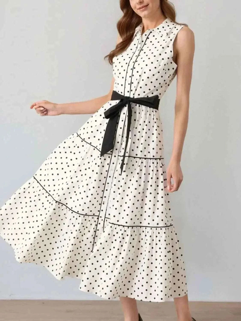 Polka Dot Sleeveless Midi Shirt Dress in white with black dots, belted waist, tiered skirt, buttoned front, and black trim detailing