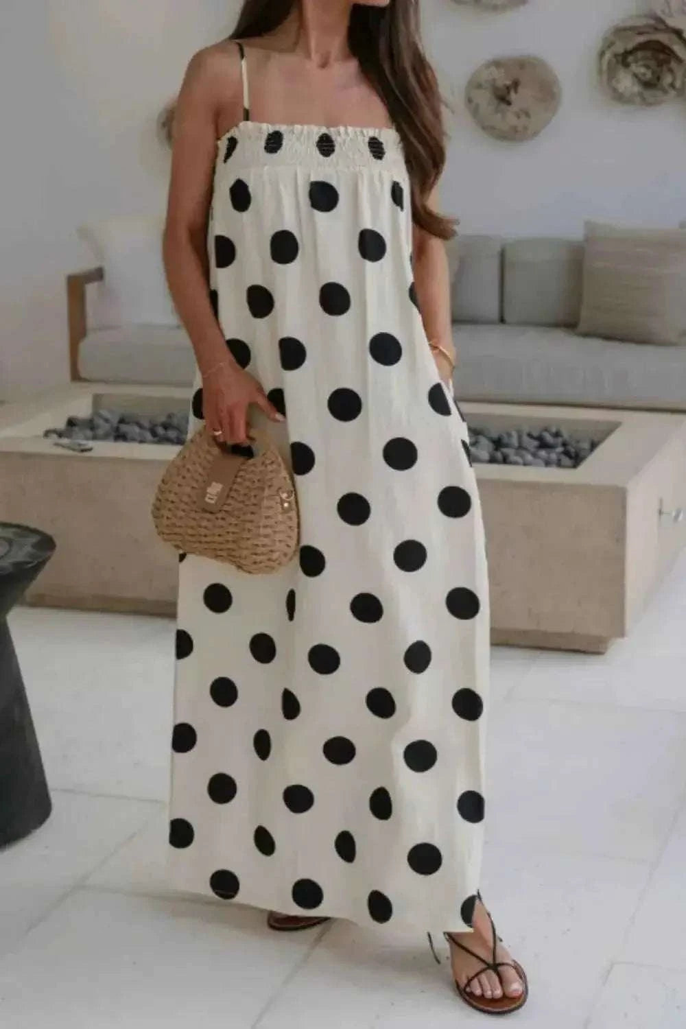 Polka Dot Spaghetti Straps Maxi Dress in white with large black polka dots, smocked bodice, and side pockets worn with sandals and a woven handbag