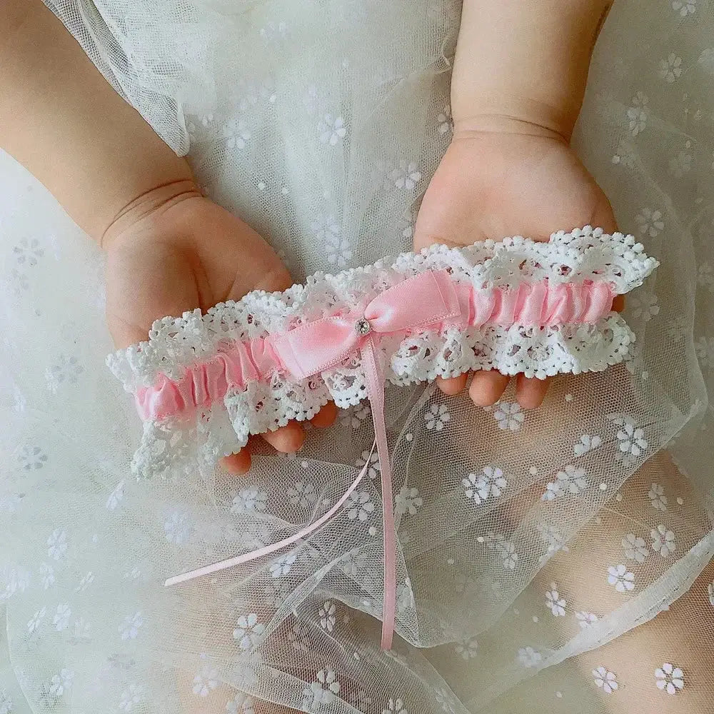 Sexy Lace Flower bridal garter belt with white lace, pink satin ribbon, and crystal embellishment held by hands