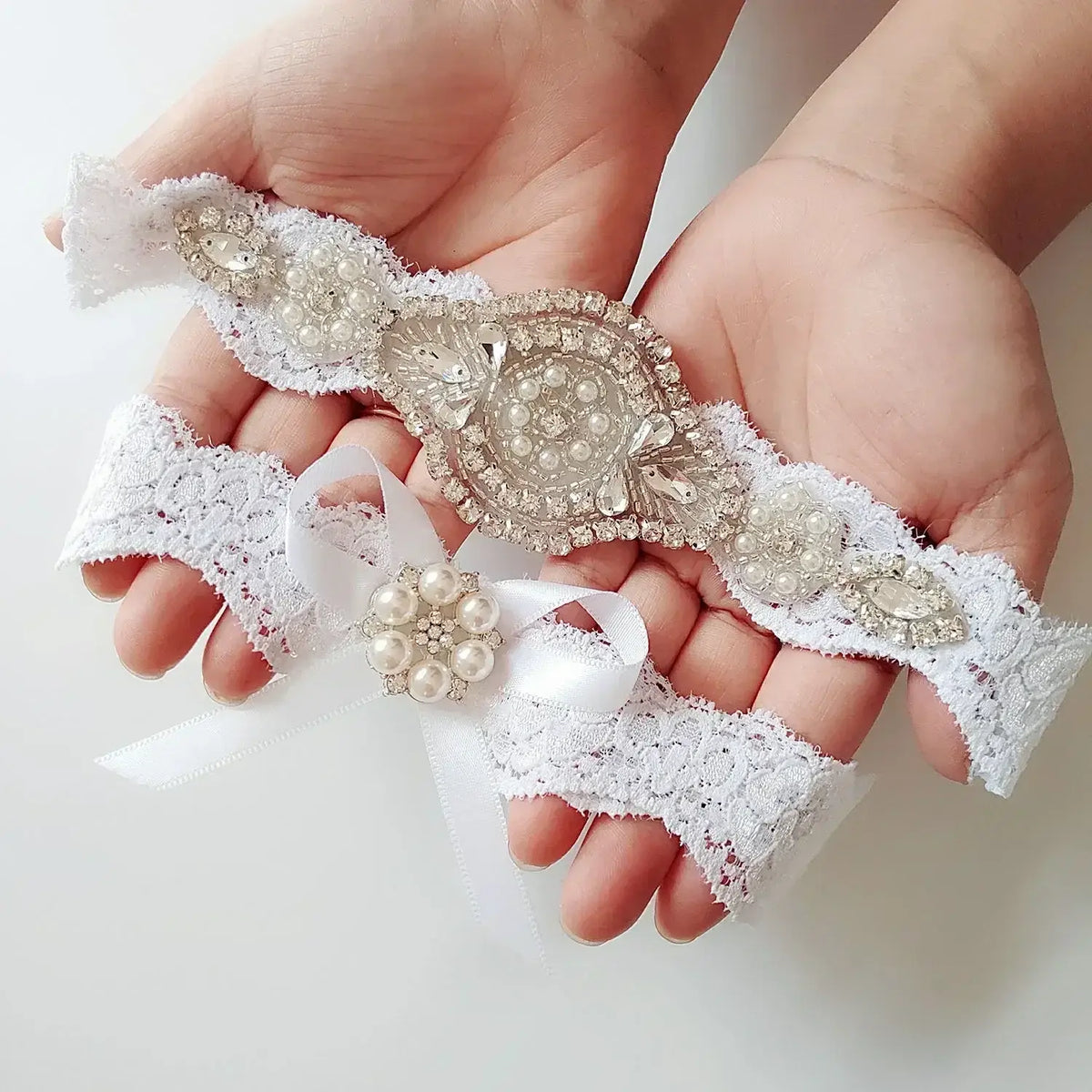 Sexy Lace Flower white lace wedding garter set with pearl and crystal appliques held in hands